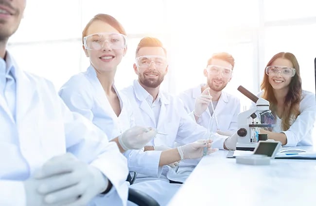 Group of people in lab coats holding devices smiling at camera