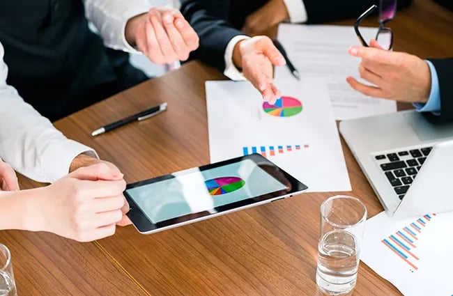 Hands gesturing around a table with various charts and graphs