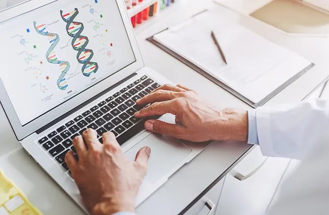 Hands typing on laptop displaying diagram of DNA double helix