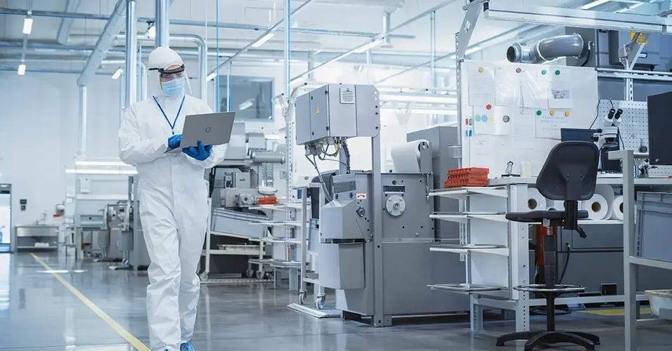 Scientist in Sterile Coverall Walking with Laptop Computer, Examining Industrial CNC Machine Settings and Configuring Production