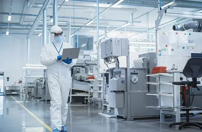 Scientist in Sterile Coverall Walking with Laptop Computer, Examining Industrial CNC Machine Settings and Configuring Production