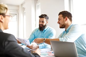 Professionals around conference table smiling pointing at papers with data graphs