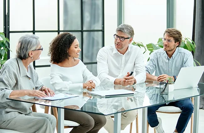 Several business professionals talking around glass conference table