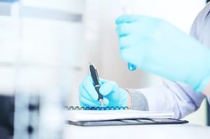 technician-observing-test-tube-writing-in-notebook