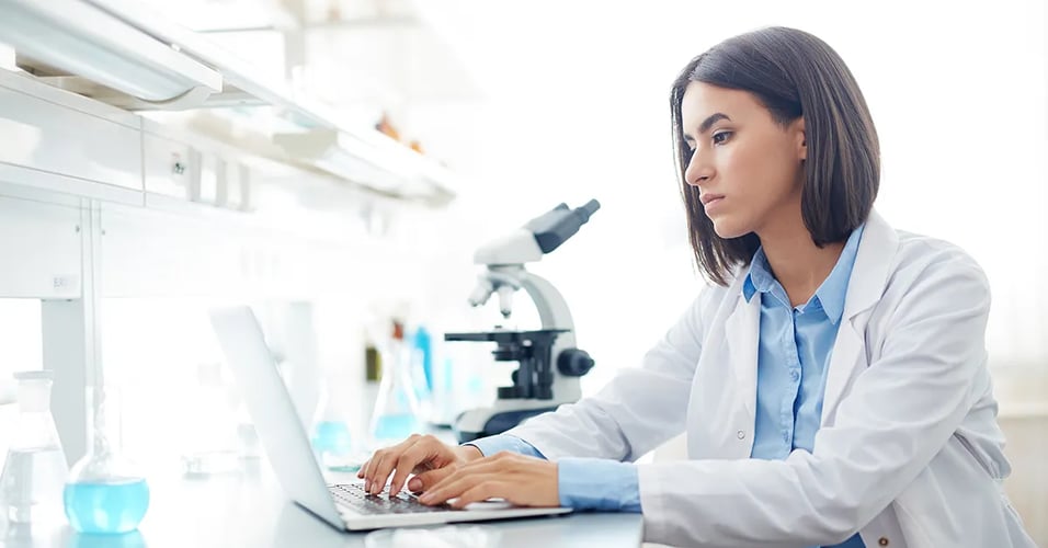 Woman in lab coat typing on laptop in a lab