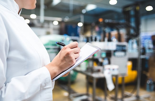 Woman writing in notebook in a manufacturing facility