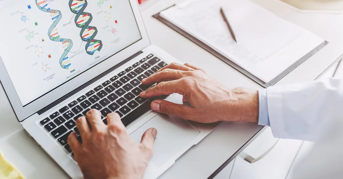 Hands typing on laptop displaying diagram of DNA double helix